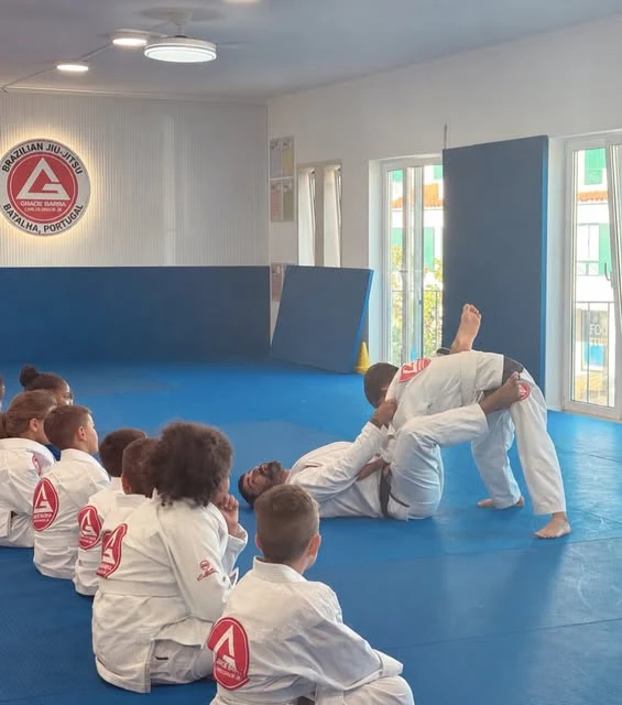 Crianças a observar uma demonstração de Jiu-Jitsu no tatame da escola